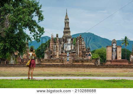 SukhothaiThailand - July 16 2017: A traveler is taking photo of old Buddhist temple in Sukhothai historical park Thailandfamous tourist attraction in notrhern Thailandselective focus at traveler at foreground and blur background.