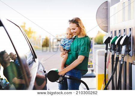 Young mother with baby boy at the petrol station refuelling the car.