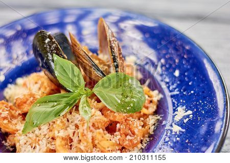 Appetizing pasta with mussels and basil. Delicious pasta frutti di mare close up. Pasta with seafood and red sauce. Delicious dinner on plate.