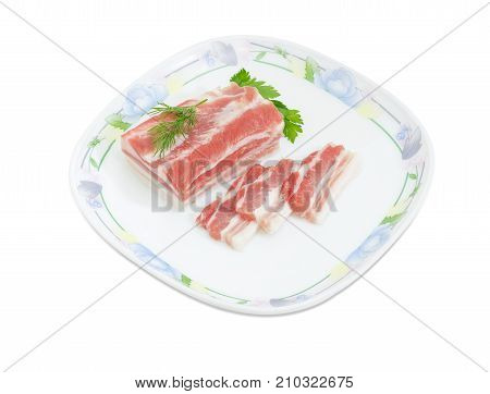 Partly sliced uncooked pork belly on dish with twigs of dill and parsley on a white background