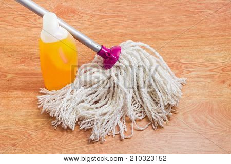 Classic mop with cotton head and metal tubular handle and plastic bottle of floor cleaner on a wooden floor