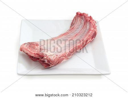 Piece of uncooked pork ribs on a square white dish on a white background