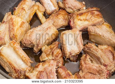 Fried pork ribs in the frying pan closeup