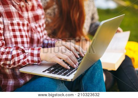 Female hands typing on laptop keyboard, woman working on computer outdoors, work anywhere concept. Beautiful young hipster woman's hands busy working on her laptop sitting