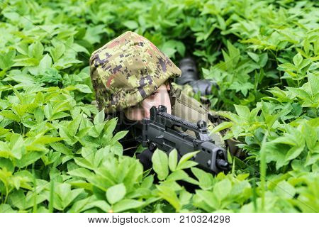 Portrait of armed woman with camouflage. Young female soldier observe with firearm. Child soldier with gun in war green goutweed background. Military army people concept