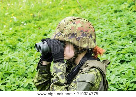 Portrait of armed woman with camouflage. Young female soldier observe with binoculars. Child soldier with gun in war green goutweed background. Military army people concept