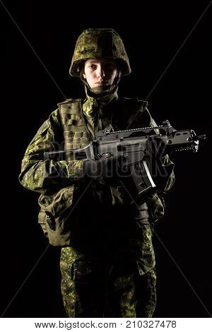 Portrait of armed woman with camouflage. Young female soldier observe with firearm. Child soldier with gun in war black background. Military army people concept