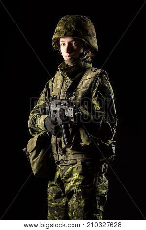 Portrait of armed woman with camouflage. Young female soldier observe with firearm. Child soldier with gun in war black background. Military army people concept