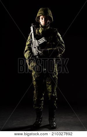 Portrait of armed woman with camouflage. Young female soldier observe with firearm. Child soldier with gun in war black background. Military army people concept