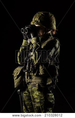 Portrait of armed woman with camouflage. Young female soldier observe with binoculars. Child soldier with gun in war black background. Military army people concept