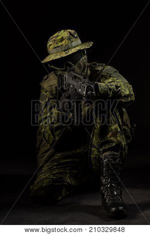 Portrait of armed woman with camouflage. Young female airsoft sniper observe with firearm. Soldier with gun in war black background. Military army people concept