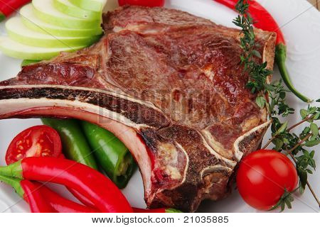 cibo di carne: arrosto nervatura sul piatto bianco con pepe timo e pomodoro sul tavolo di legno