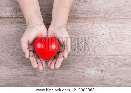 Love Concept : Woman Hands Holding Red Heart On Brown Wooden Table. Free Space For Text