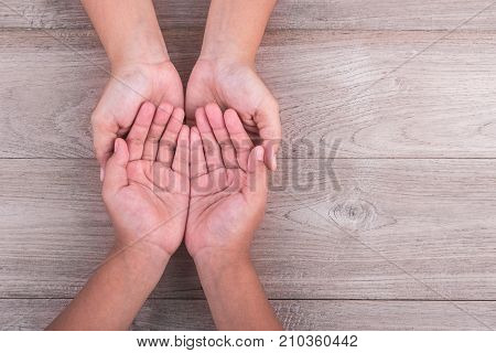 Help And Support Concept : Woman Holds Her Young Kids Hands On Brown Wooden Table. Free Space For Te