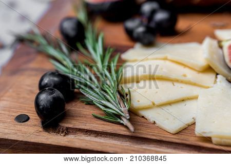 Close up tasty dinner concept with cheese, olives and rosemary on wooden board