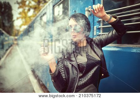 Elegant woman smoking e-cigarette with smoke wearing suit and hat