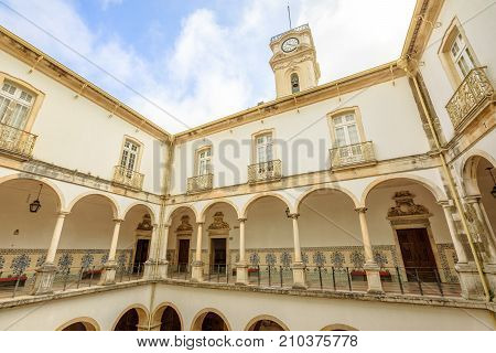Coimbra, Portugal - August 14, 2017: cloister inside University of Coimbra, the Europe's oldest university founded in 1290. Iconic Clock Tower on background, a important tourist attraction in Coimbra.