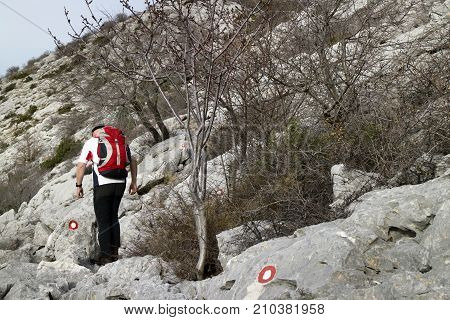 Climber with red backpack following the markings on the hard rocky terrain on the mountain Mosor in Croatia