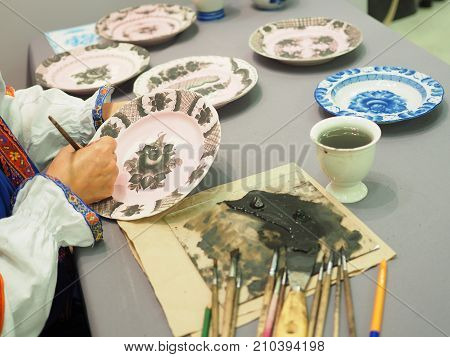 Woman paints a ceramic plate. National craft