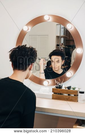 Attractive woman primp at the mirror with lamps in the beauty studio. A happy satisfied customer of make-up and hairstyle service.