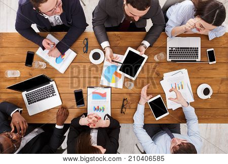 Multiethnic company meeting. Manager and emploees work in comfortable office, discuss the report, top view of wooden table