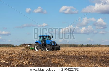a large blue tractor plowing field against the beautiful sky. Work of agricultural machinery. Harvest