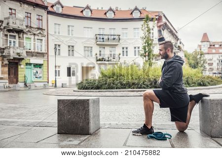 Millenial slim man streching his body in a city site. After-training routine.