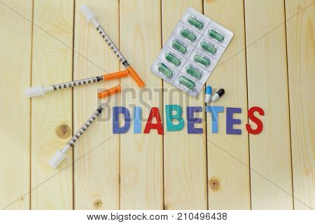 Word DIABETES with medication and insulin syringe on wooden table