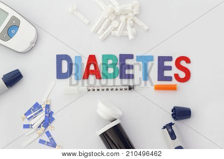 Word DIABETES with insulin syringe,lancet,test strip,glucose meter and lancing device on isolated white background