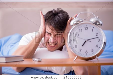 Man in bed frustrated suffering from insomnia with an alarm cloc