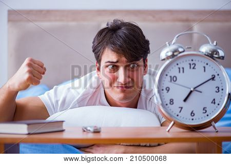Man in bed frustrated suffering from insomnia with an alarm cloc