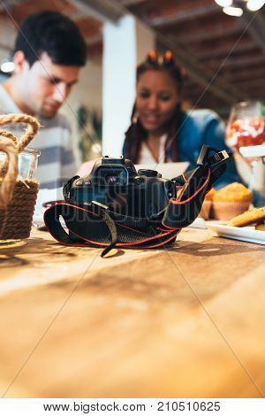 Photo camera in the foreground and young mixed race woman and caucasian young man photographers co-working at the background