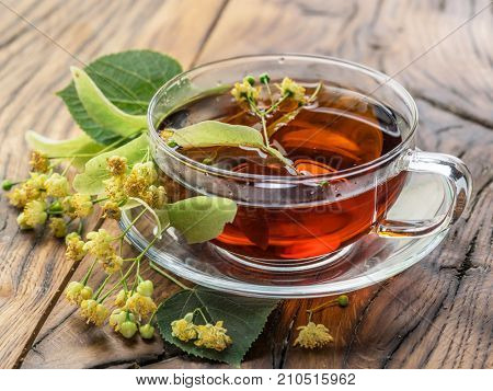 Cup of linden tea and lime flowers on the wooden table.