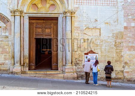 SPELLO, ITALY - MAY 27 2017 - Three people watch the program of the celebrations of the Blessed Virgin Mary in front of the entrance of the church of Spello Umbria.