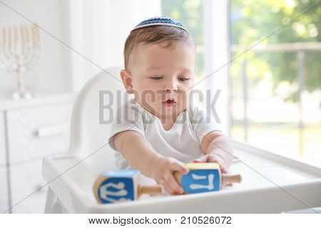 Cute baby in kippah playing with dreidels while sitting on high chair