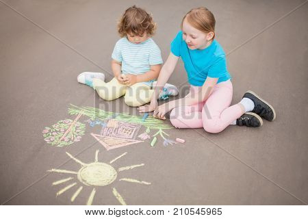 Little girls sisters chalking at the asphalt. Friendship childhood elder sister. Best friends children. Drawing with color chalk. Kids in kindergarten. Preschooler leisure time. Artistic talented kids. Children's drawings.