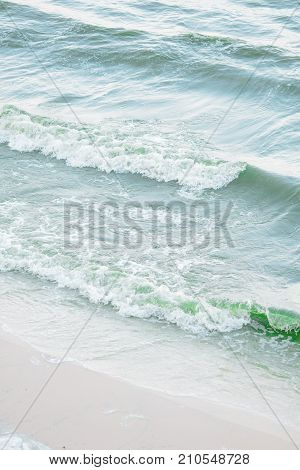 Blue ripples waving towards sand beach shore from side view for summer and vacation background
