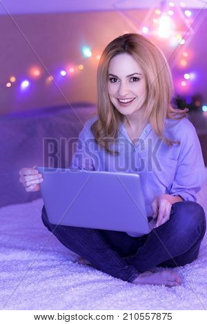 I feel happy. Happy attractive dark-eyed lady smiling while sitting on the sofa and holding her laptop