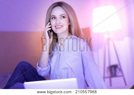 Pleasant talk. Happy beautiful blond woman smiling and talking on the phone while sitting