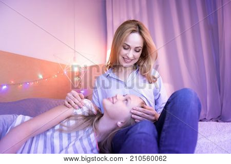 My precious. Happy loving devoted mom caressing her daughter and looking at her while the girl relaxing on her lap