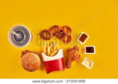 Fast food dish top view. Meat burger, potato chips and chicken. Take away composition. French fries, hamburger, mayonnaise and ketchup sauces on yellow background. Menu or receipt background