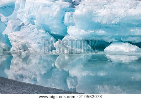 Blue growler piece of iceberg with reflection in calm water. Global warming, melting of ice. Arctic ocean
