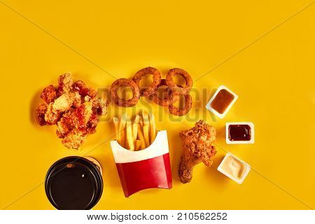 Fast food dish top view. Meat burger, potato chips and chicken. Take away composition. French fries, hamburger, mayonnaise and ketchup sauces on yellow background. Menu or receipt background