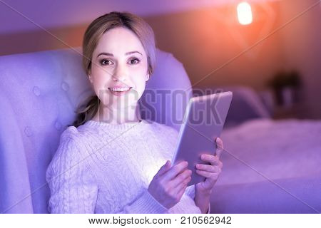 Over the moon. Good-looking dark-eyed blond lady beaming with happiness and her eyes shining while holding the tablet