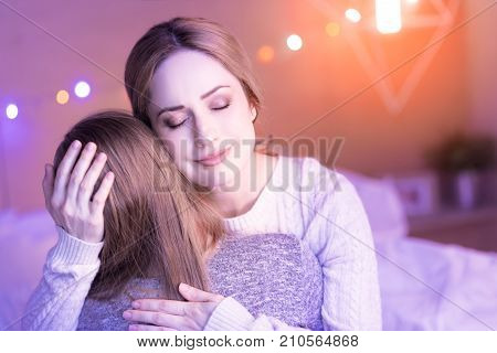 My treasure. Content loving caring mom smiling and touching her childs head while hugging her daughter