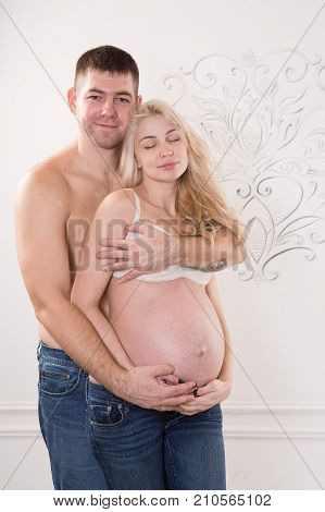Beautiful pregnant couple in love on the background. Hands of husband on the tummy of his pregnant wife. Young man tenderly stroked pregnant belly of his wife. Husband kissing pregnant belly.