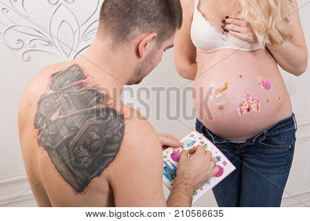 Beautiful pregnant couple in love on the background. Hands of husband on the tummy of his pregnant wife. Young man tenderly stroked pregnant belly of his wife. Husband kissing pregnant belly.