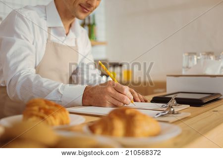 Paper work. Handsome nice smart man standing in the kitchen and taking notes while working with papers