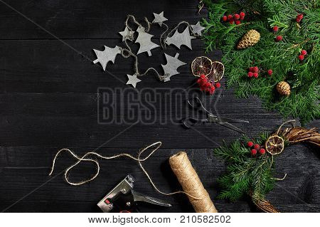Make a Christmas wreath with your own hands. Spruce branch, Christmas wreath and gifts on a black wooden background. Workplace for preparing handmade decorations.