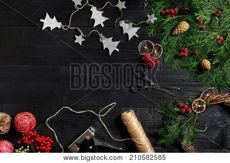 Make a Christmas wreath with your own hands. Spruce branch, Christmas wreath and gifts on a black wooden background. Workplace for preparing handmade decorations.